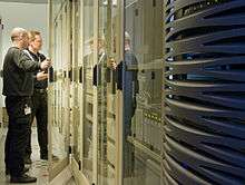 Two men standing in front of a bank of computers