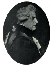  Right profile of stern-faced man in dark clothing with lacy shirt and cuffs, wearing a wig