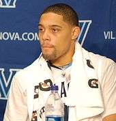 An African American with short hair and goatee sits with a towel at a press conference.