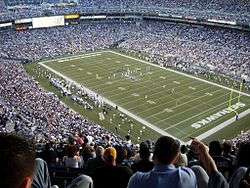 A stadium filled with spectators with two football teams on the field between a play.