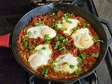 Shakshouka with five cooked eggs on top of tomato sauce in cast iron skillet