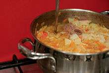 A metal pot filled with cabbage soup and a chunk of meat