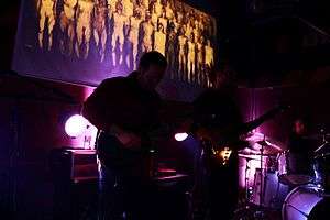 Snovi band performing on stage, spotlit, with a video projection in the background