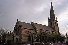 A church with bands of differently coloured stone, and a tower with a spire supported by flying buttresses