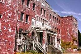 Exterior view of the abandoned and decrepit, red brick building that formally housed the St. Michael's Residential School in Alert Bay, British Columbia. Peeling paint is visible over the entirety of the building