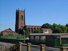 A church seen from the south with a west tower surmounted by a pierced parapet and pinnacles