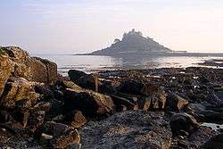 An island surrounded by water and rocks in the foreground