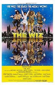 Four characters from the film dancing on top of a logo "THE WIZ". A city skyline just after dusk is seen behind them, and the entire scene is mirrored in water before them. The people are Dorothy, the Scarecrow, the Tin Woodman, and the Lion.