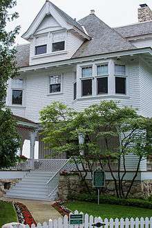 A medium-sized four-story house with wooden siding and a covered porch on the first floor.