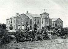 A black and white photohraph of a large mansion house, surrounded by various trees around it.