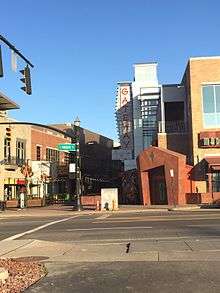 A view across a signalized intersection, with a green sign opposite reading "High Street", to some buildings with an irregular, stylized entrance on one side of a pedestrian mall, lit by low raking sunlight. In the rear is a sign with "Gateway" on it in vertical red letters.