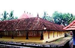 Low, square building with a decorated wood-shingle roof