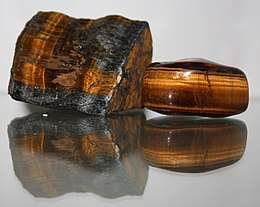 A photograph showing a polished reddish brown stone which is bisected by a band containing golden fibers