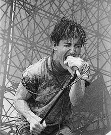 A man caked in mud screaming into a microphone.