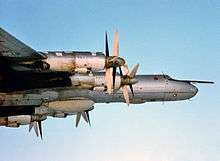 Sideview of aircraft in-flight powered by turboprops, whose huge propellers are apparent.