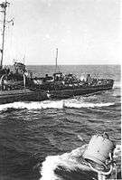 The doctor of Chaffee is suspended on a line between the Chaffee and another ship. He is being pulled along the line in a harness referred to as a "breeches buoy".