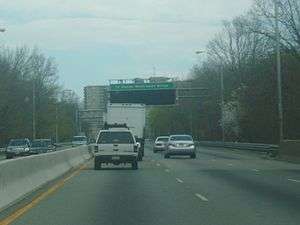 A four-lane freeway in an urbanized area. An overhead sign in the distance reads To George Washington Bridge with a blank variable message sign below it.