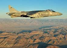 Side view of fighter jet flying above mountain range