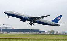 Boeing 7777 airliner taking off. The jet's nose is angled upwards as it lifts above the runway, with landing gear still deployed.