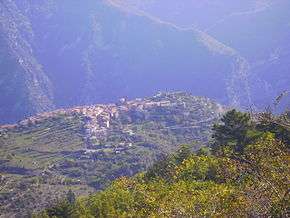 Photo looking down a town situated on a high plateau amid tree-covered mountains