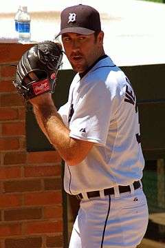 A man in a white baseball uniform and a black cap with a "D" on it prepares to pitch.