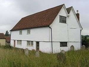 A white building with a red-tied roof seen from an angle and looking more like a house than a chapel. It has two storeys, a double gable, two windows on the end and on the entrance front are two doors and two windows in each storey.