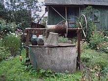 house and flowers in background, large water well in foreground