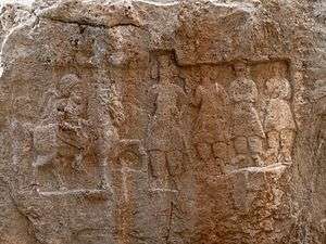 Faded relief carved into the side of a rock. The scene portrays a man on horseback as well as several other characters.