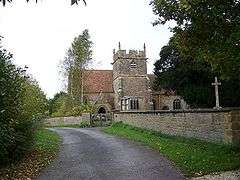 Stone building with square tower separated from the road in the foreground by a stone wall.