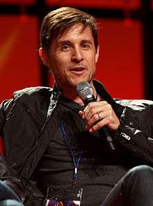 This is a picture of Yuri Lowenthal who is talking with a microphone.