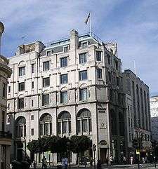 An Edwardian building with six floors stands on a moderate day, a flag flying atop it.