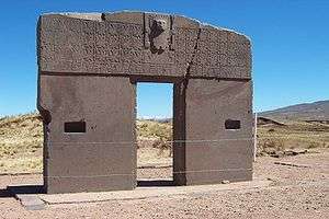 Simple stone gate decorated with a flat repeating checkered pattern of small figures and a larger figure in relief at the center top.