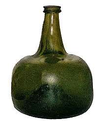 A squat semi-transparent green blown glass bottle, shaped vaguely like a squarish mandarin citrus, with a strongly concave base and a short flanged neck.